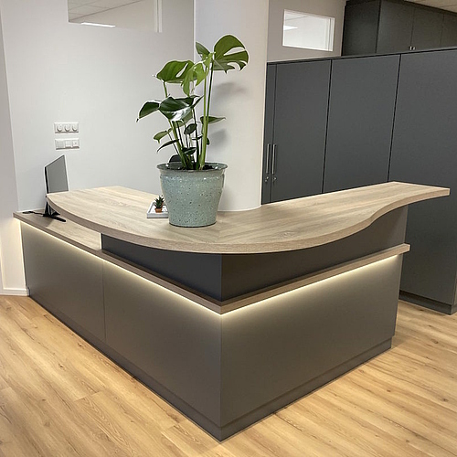 Moderne Empfangstheke aus Schichtstoff in Anthrazit mit abgerundetem Thekenbrett – maßgefertigte Praxismöbel und Ladenbau von Hofmann, auch für Gastro Möbel geeignet.